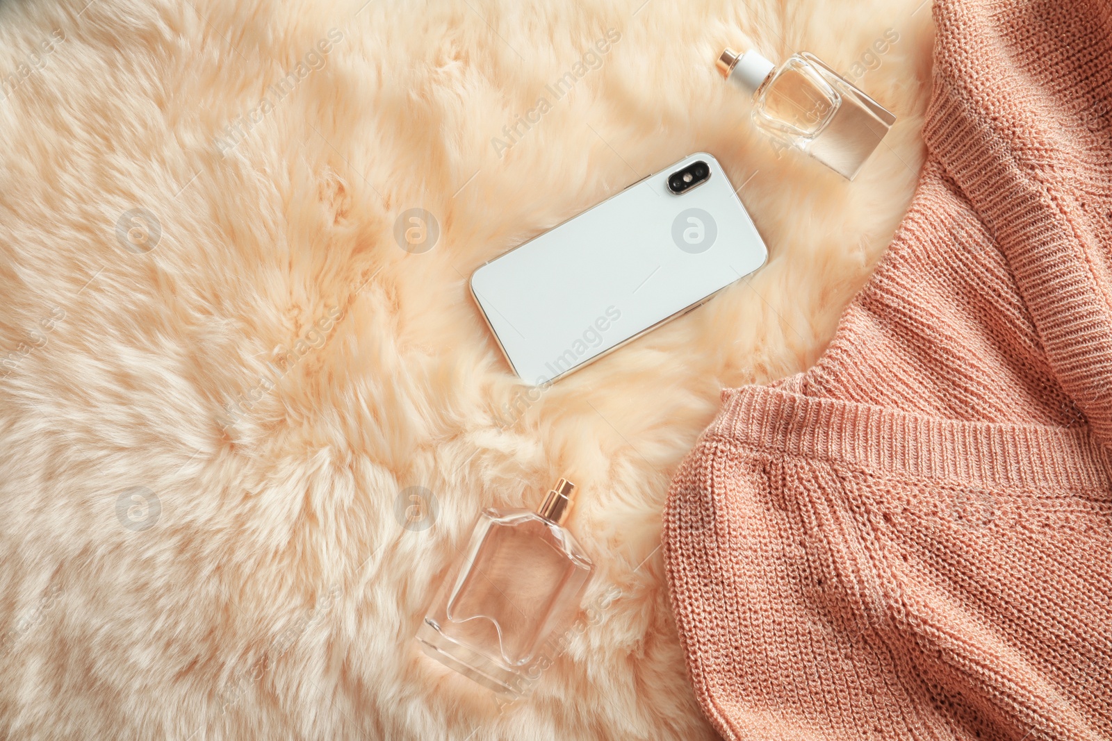 Photo of Flat lay composition with warm knitted clothes, smartphone and perfume on faux fur