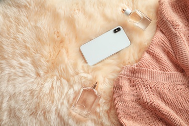 Photo of Flat lay composition with warm knitted clothes, smartphone and perfume on faux fur