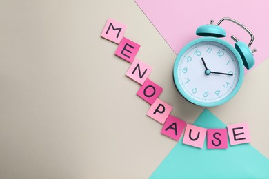 Photo of Pink paper notes with word Menopause and alarm clock on color background, flat lay. Space for text