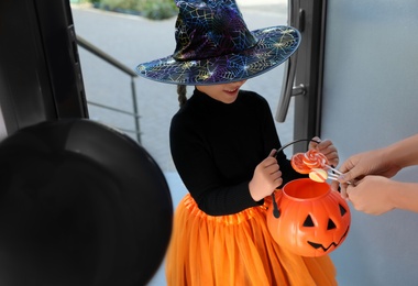 Photo of Cute little girl dressed as witch trick-or-treating at doorway. Halloween tradition