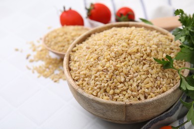 Photo of Raw bulgur in bowl and parsley on white table, closeup