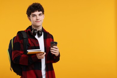 Portrait of student with backpack, headphones and notebooks on orange background. Space for text