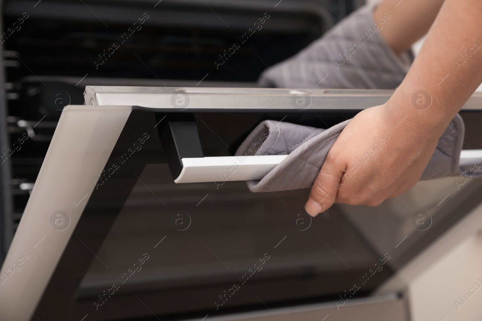 Photo of Woman putting baking tray into electric oven, closeup