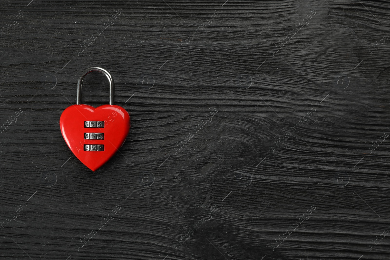 Photo of Red heart shaped combination lock on black wooden table, top view. Space for text