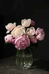 Bouquet of beautiful peonies in glass vase on dark table against black background