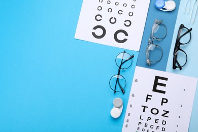Photo of Vision test charts, glasses, lenses and tweezers on light blue background, flat lay. Space for text