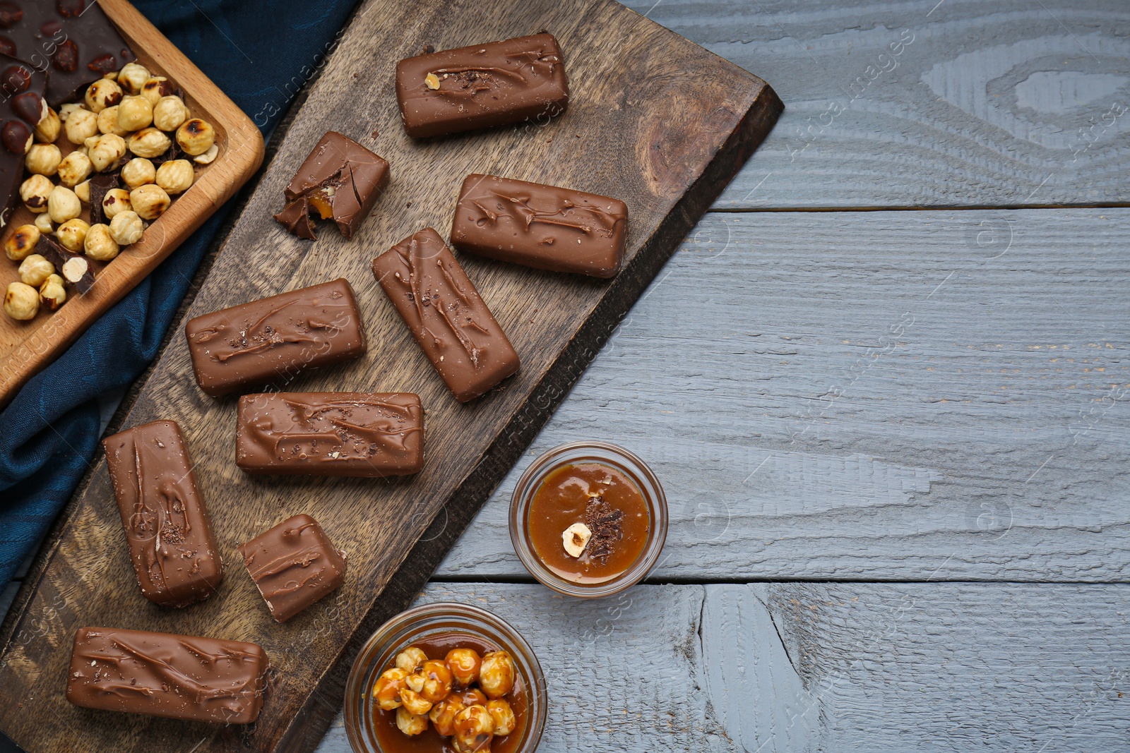 Photo of Delicious chocolate candy bars with caramel and nuts on grey wooden table, flat lay. Space for text