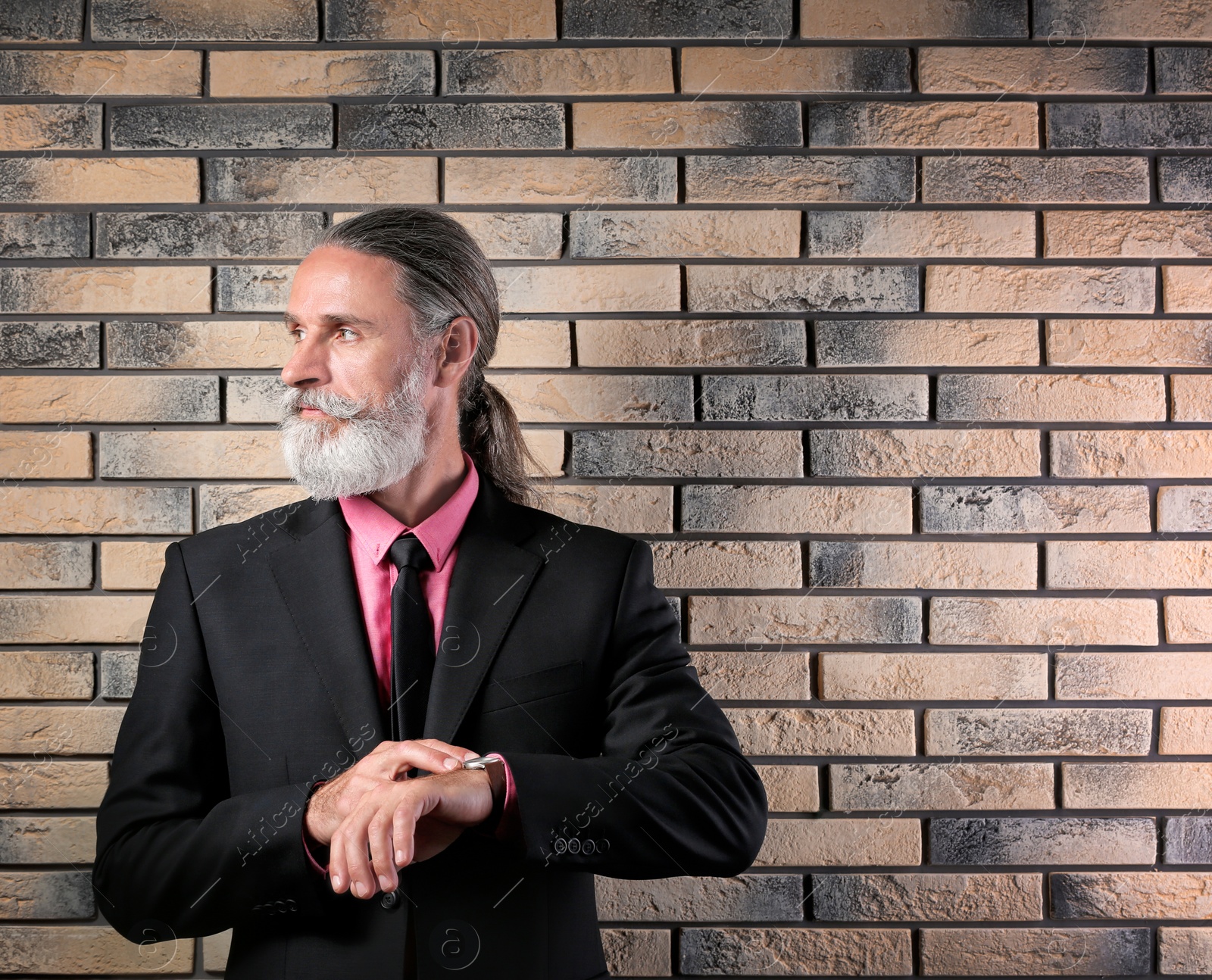 Photo of Handsome bearded mature man in suit near brick wall background