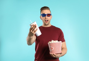 Emotional man with 3D glasses, popcorn and beverage during cinema show on color background