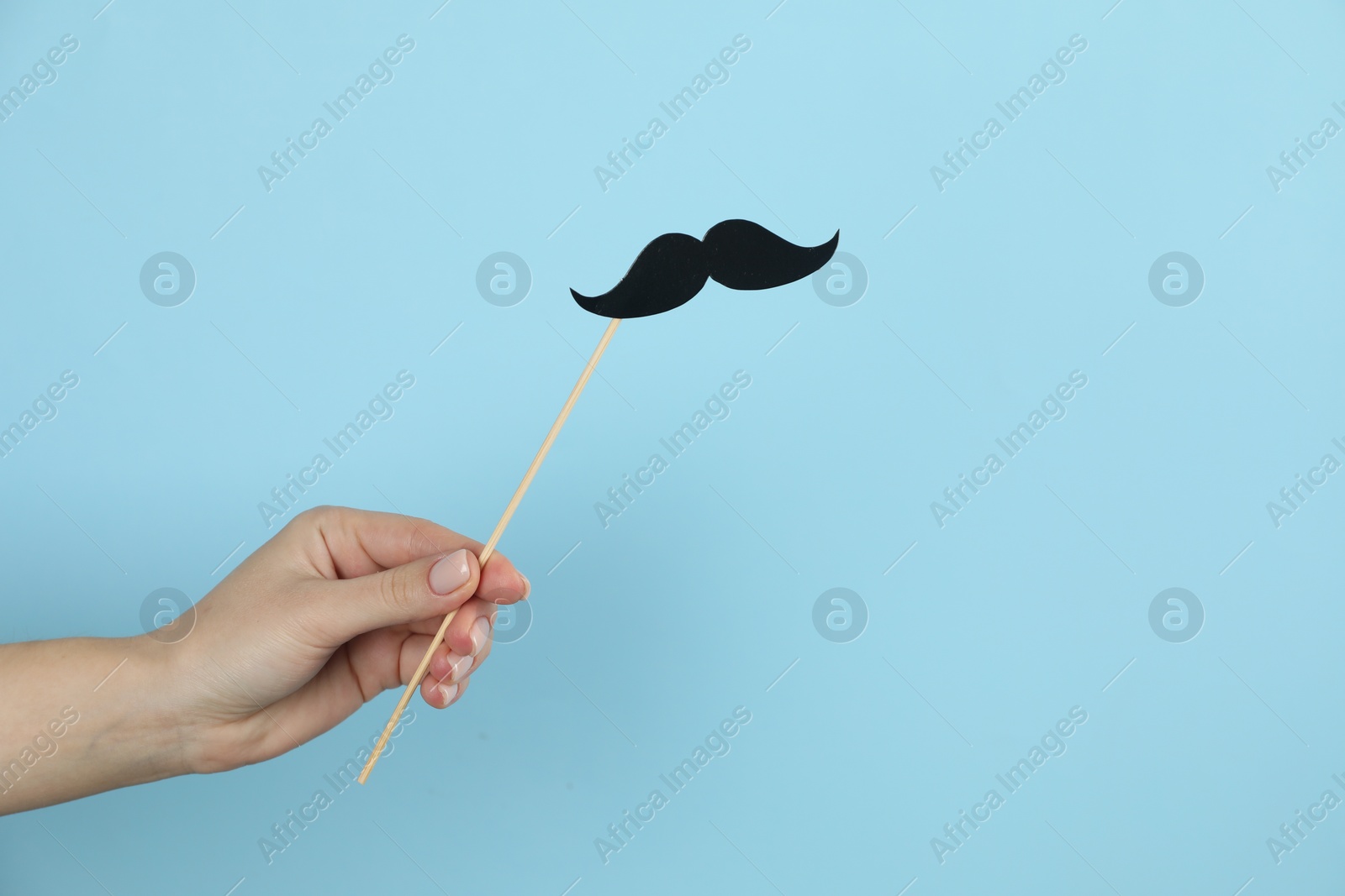 Photo of Woman with fake paper mustache on light blue background, closeup. Space for text