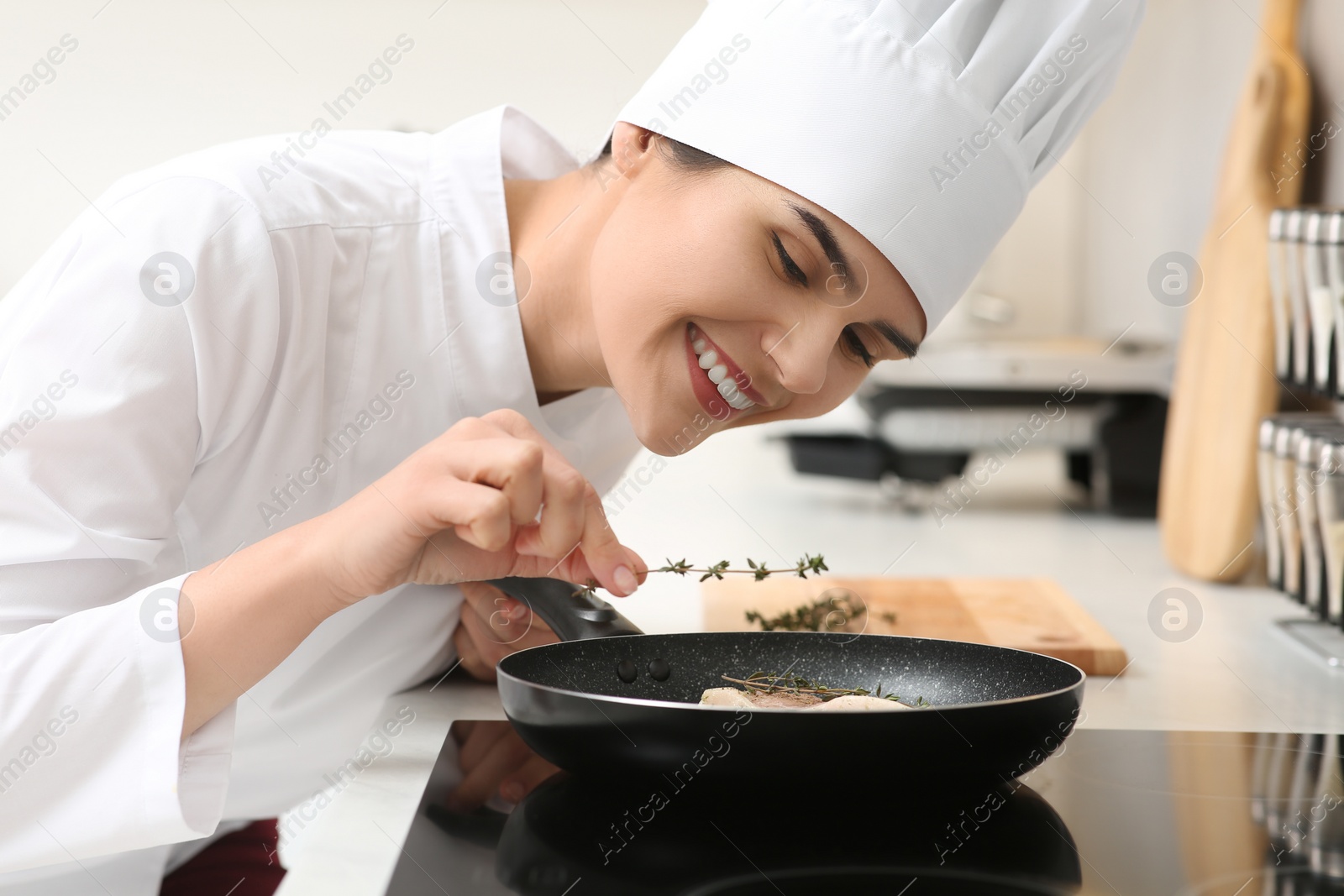 Photo of Professional chef adding thyme into frying pan in kitchen