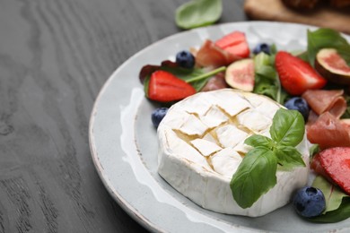 Photo of Delicious salad with brie cheese, blueberries, figs and strawberries on grey wooden table, closeup