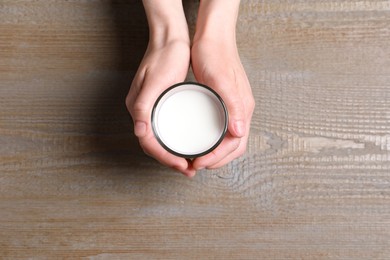 Photo of Woman holding glass of milk at wooden table, top view