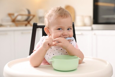 Photo of Cute little baby eating food in high chair at kitchen