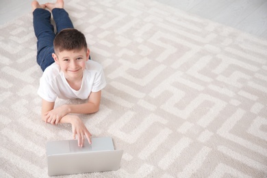 Happy boy with laptop lying on cozy carpet at home