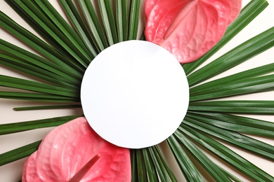 Photo of Creative composition with tropical flowers, green foliage and card on light background, top view