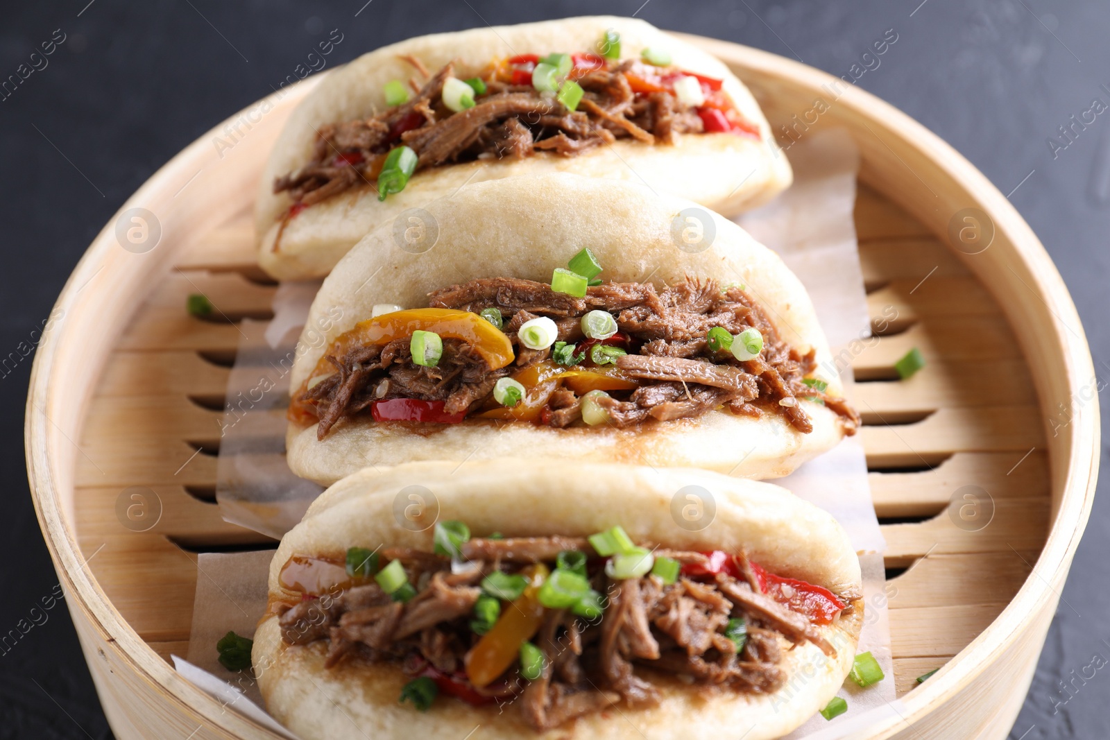 Photo of Delicious gua bao in bamboo steamer on black table, closeup