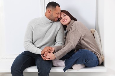 Photo of Dating agency. Happy couple holding hands and sitting on window sill at home