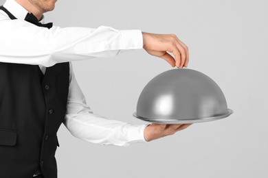 Photo of Waiter holding metal tray with lid on light background