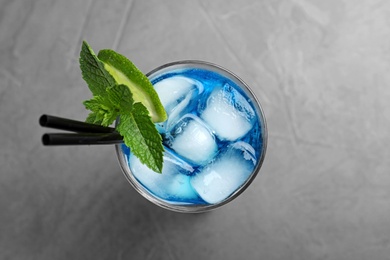 Glass of tasty refreshing cocktail with mint and lime on grey background, top view