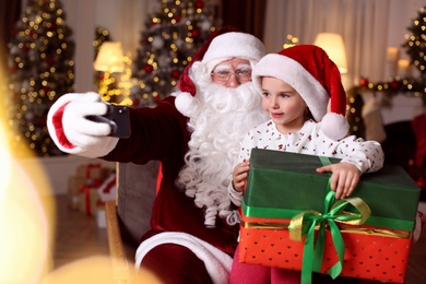 Santa Claus and little girl taking selfie in room decorated for Christmas