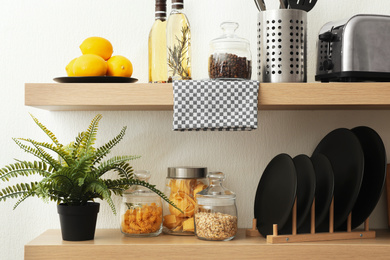 Photo of Wooden shelves with dishware and products on white wall. Kitchen interior idea