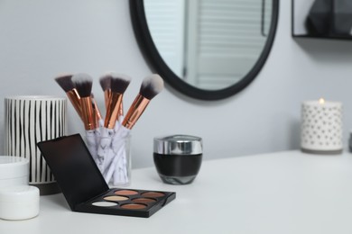 Stylish round mirror hanging above dressing table, focus on cosmetic products. Space for text