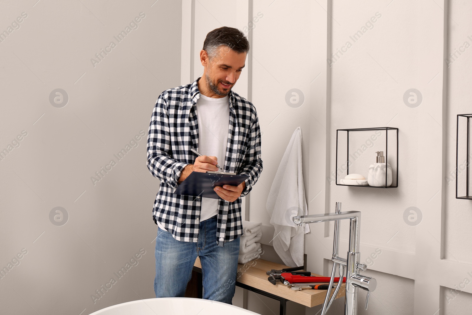 Photo of Plumber with clipboard checking water tap in bathroom