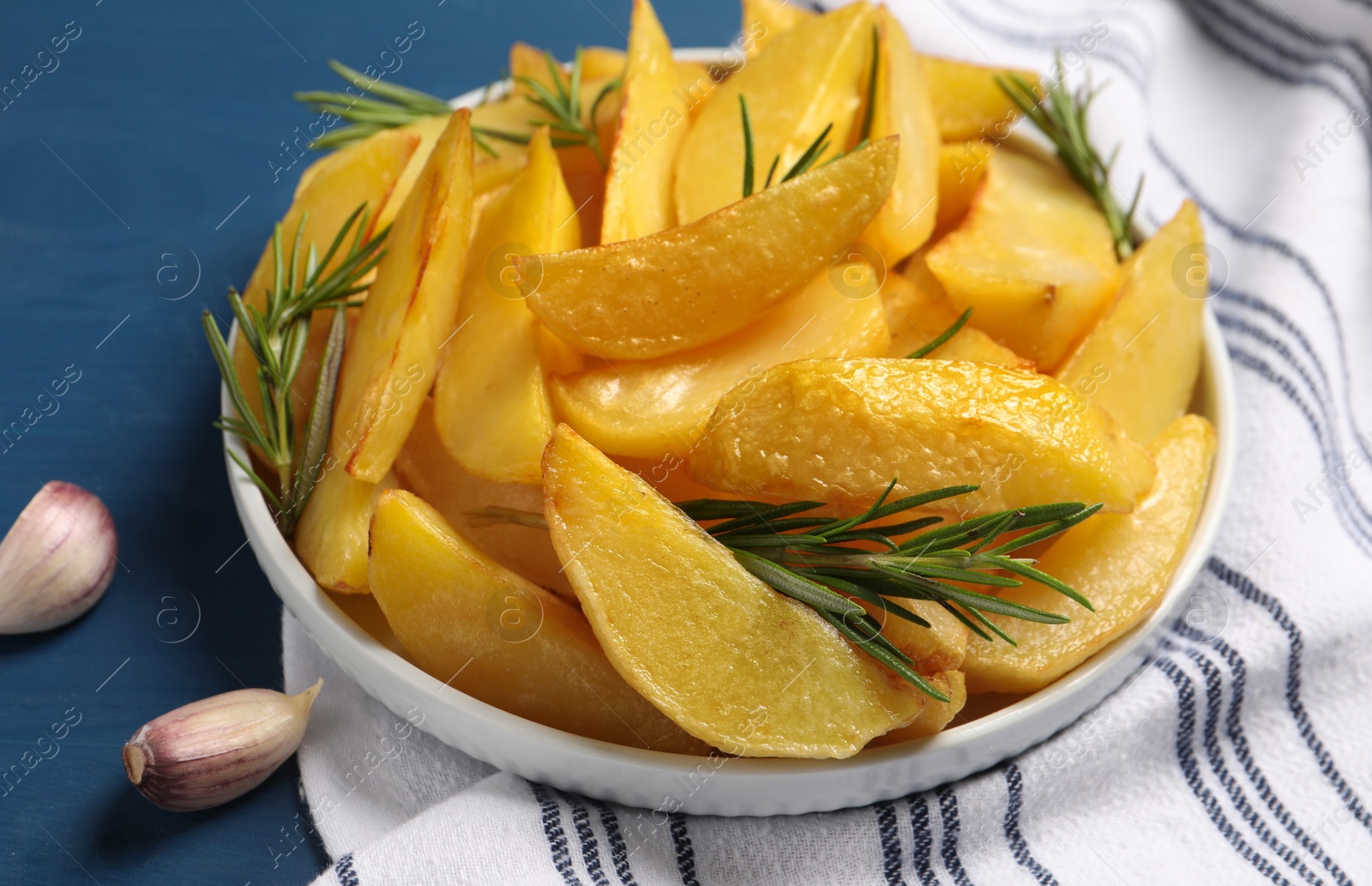 Photo of Plate with tasty baked potato wedges and rosemary on blue wooden table, closeup