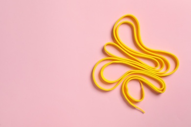 Photo of Yellow shoelace on pink background, top view. Space for text
