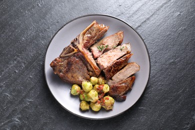 Delicious fried beef meat, vegetables and thyme on black table, top view