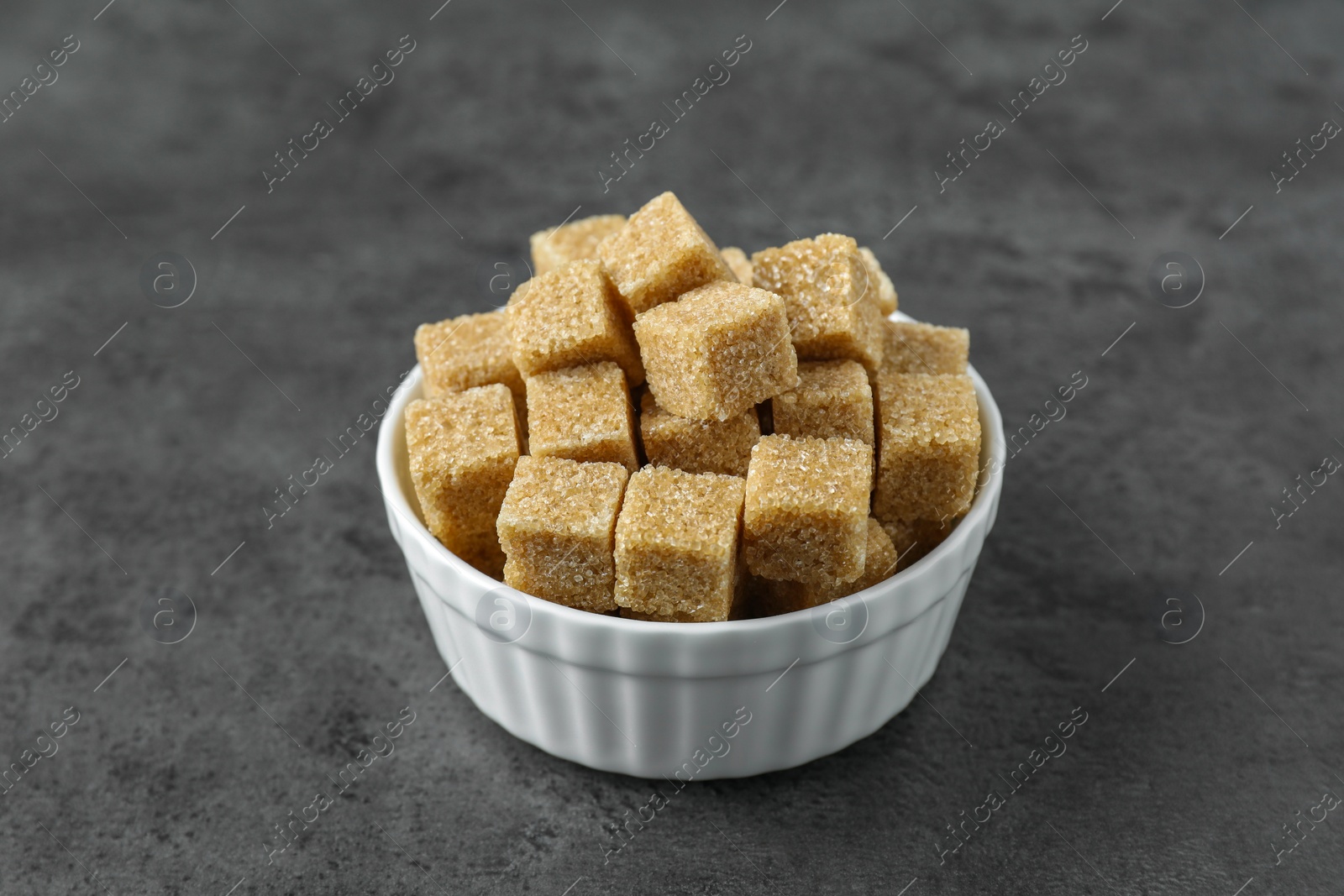 Photo of Brown sugar cubes in bowl on grey table