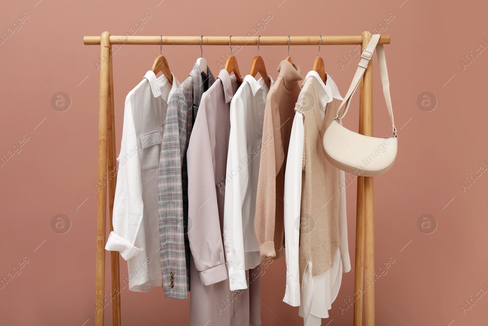 Photo of Rack with different stylish clothes and bag on pale pink background