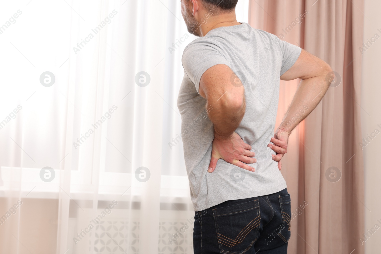 Photo of Man suffering from back pain indoors, closeup