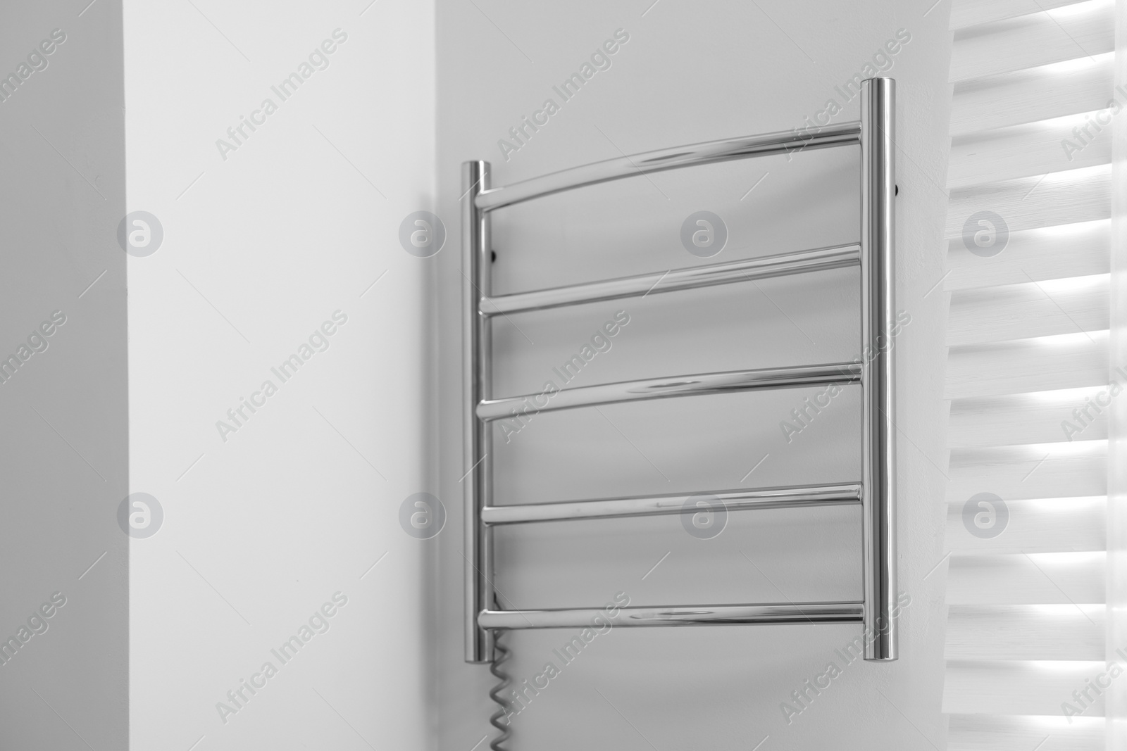 Photo of Heated towel rail on white wall in bathroom