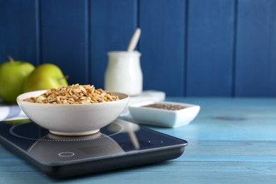 Photo of Electronic scales with granola on light blue wooden table, space for text