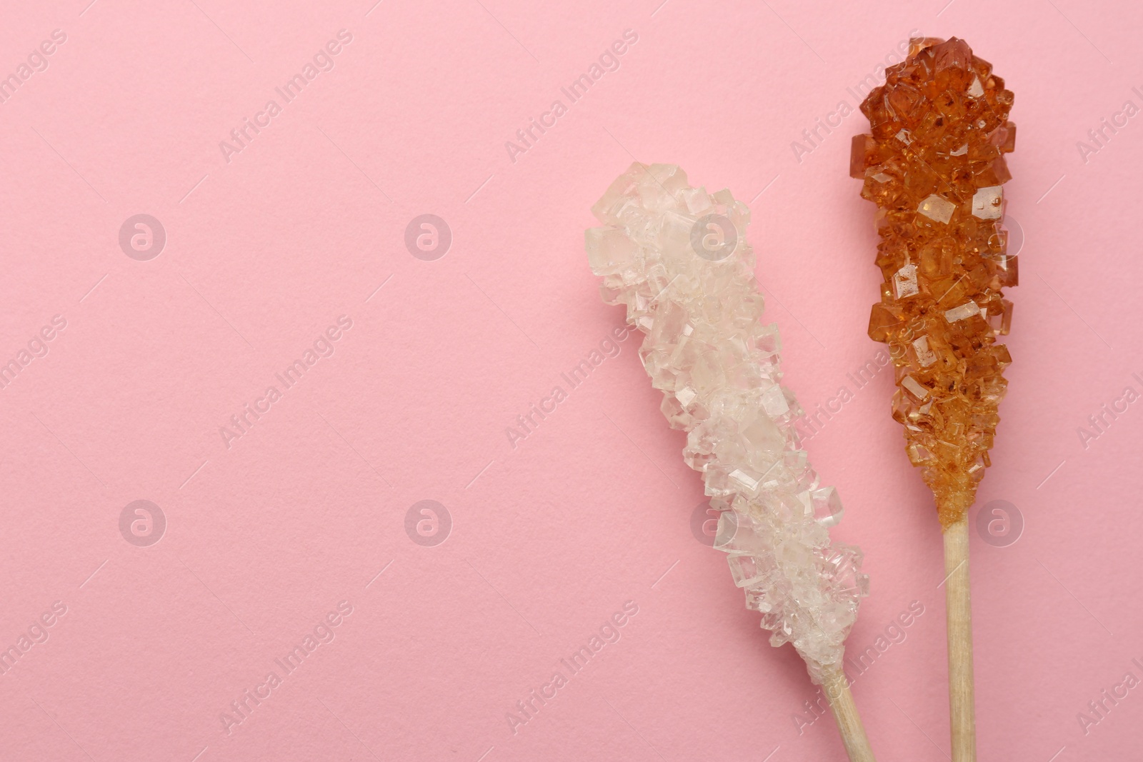 Photo of Wooden sticks with sugar crystals and space for text on pink background, flat lay. Tasty rock candies