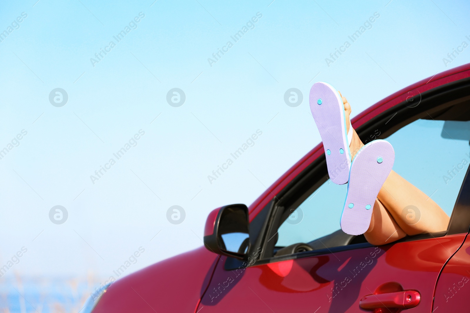 Photo of Closeup of woman showing legs with flip flops from car, space for text. Beach accessories