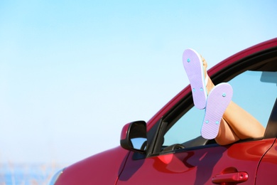 Photo of Closeup of woman showing legs with flip flops from car, space for text. Beach accessories