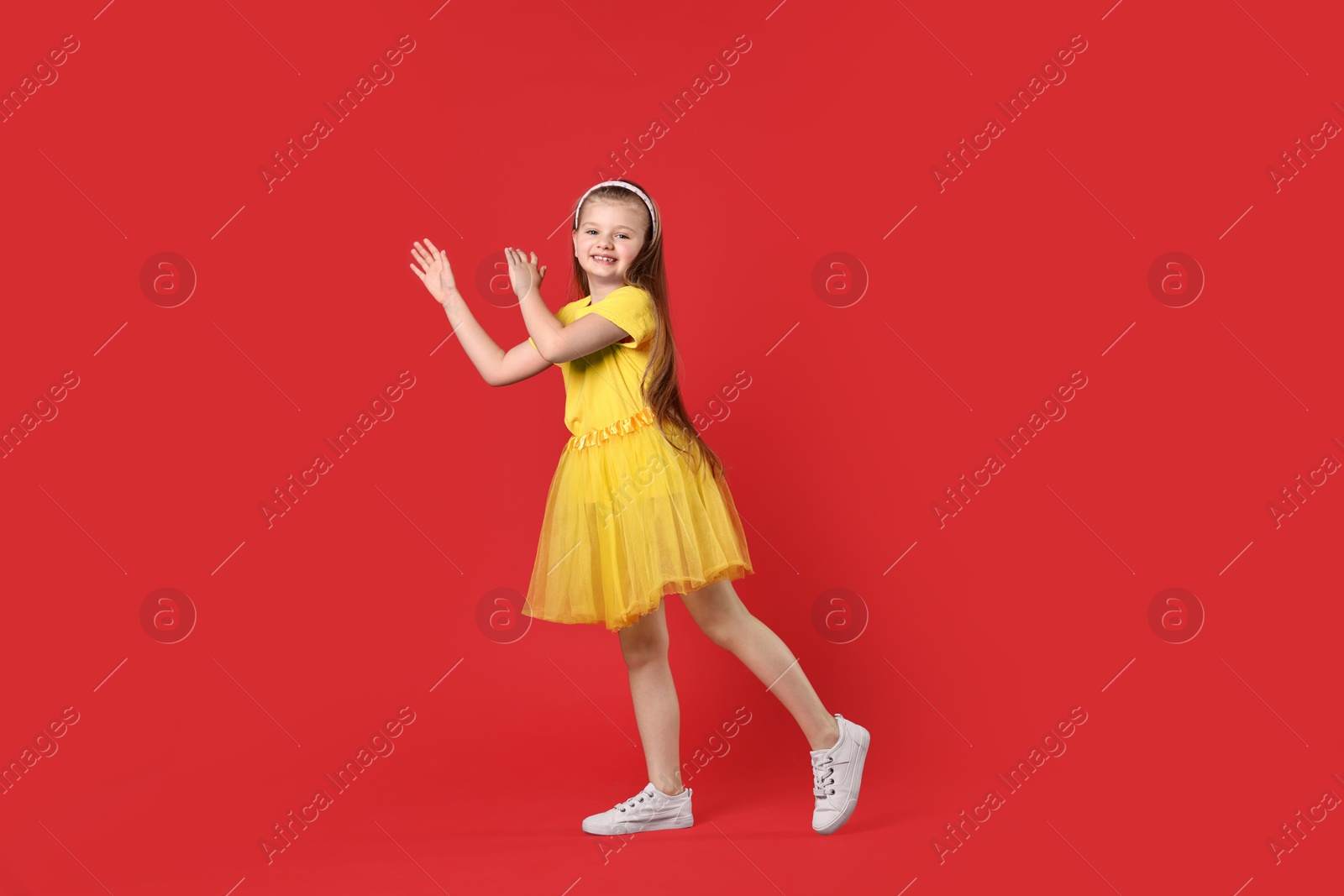 Photo of Cute little girl dancing on red background