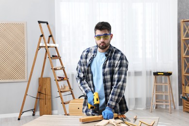 Photo of Young handyman working with electric drill at table in workshop