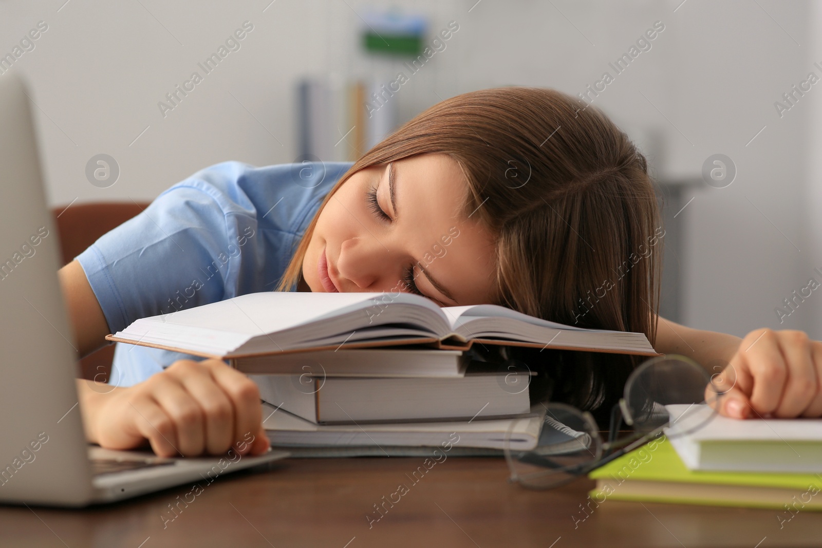 Photo of Young tired woman sleeping near books at wooden table indoors