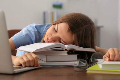 Young tired woman sleeping near books at wooden table indoors