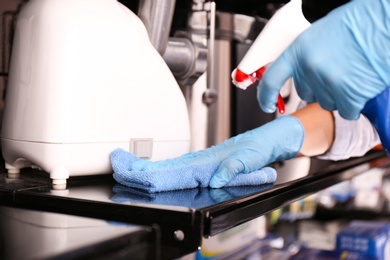 Photo of Woman cleaning shelf with rag and detergent in electronic store, closeup