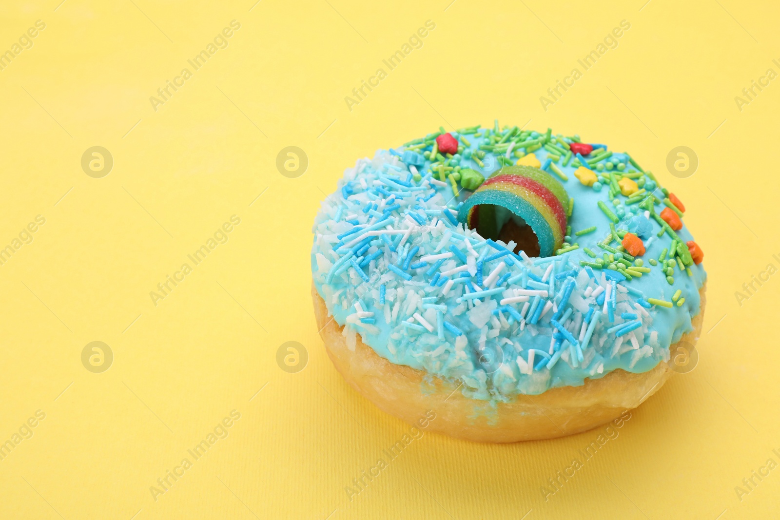 Photo of Glazed donut decorated with sprinkles on yellow background, closeup. Space for text. Tasty confectionery