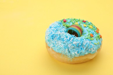 Photo of Glazed donut decorated with sprinkles on yellow background, closeup. Space for text. Tasty confectionery