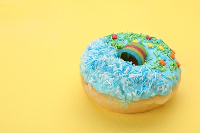 Glazed donut decorated with sprinkles on yellow background, closeup. Space for text. Tasty confectionery