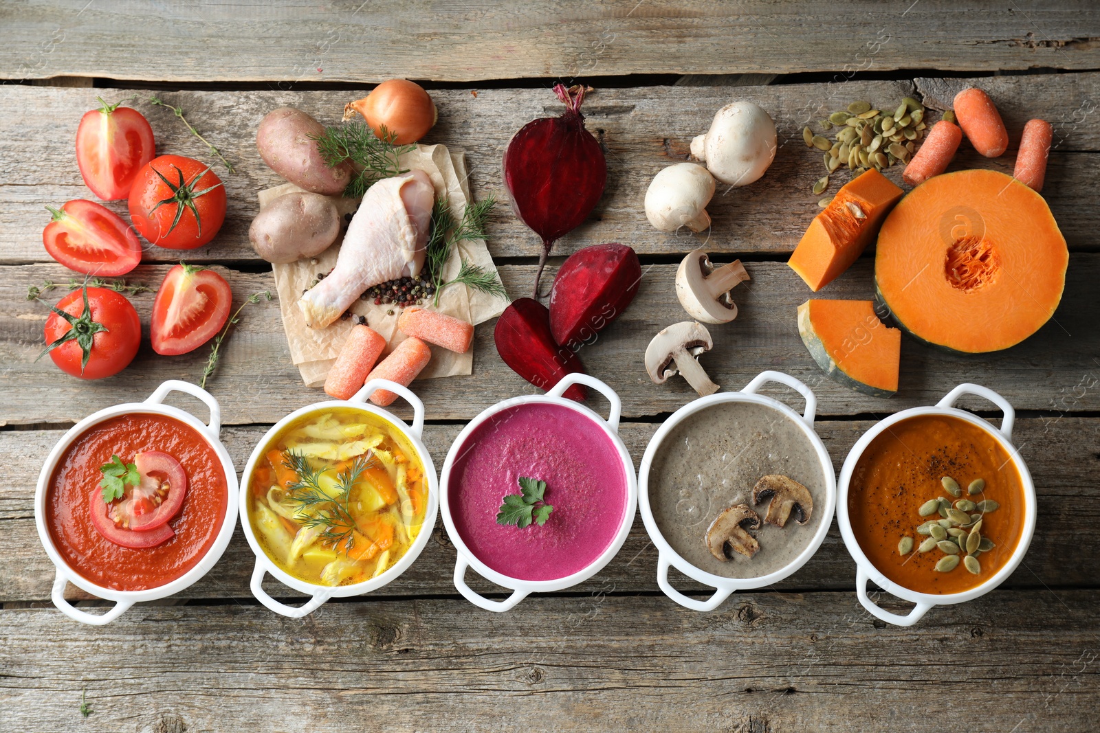 Photo of Tasty broth, different cream soups in bowls and ingredients on old wooden table, flat lay