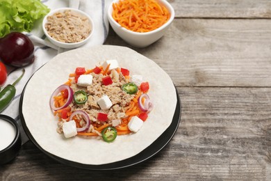 Delicious tortilla with tuna, vegetables and cheese on wooden table, space for text. Cooking shawarma