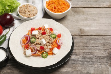 Photo of Delicious tortilla with tuna, vegetables and cheese on wooden table, space for text. Cooking shawarma